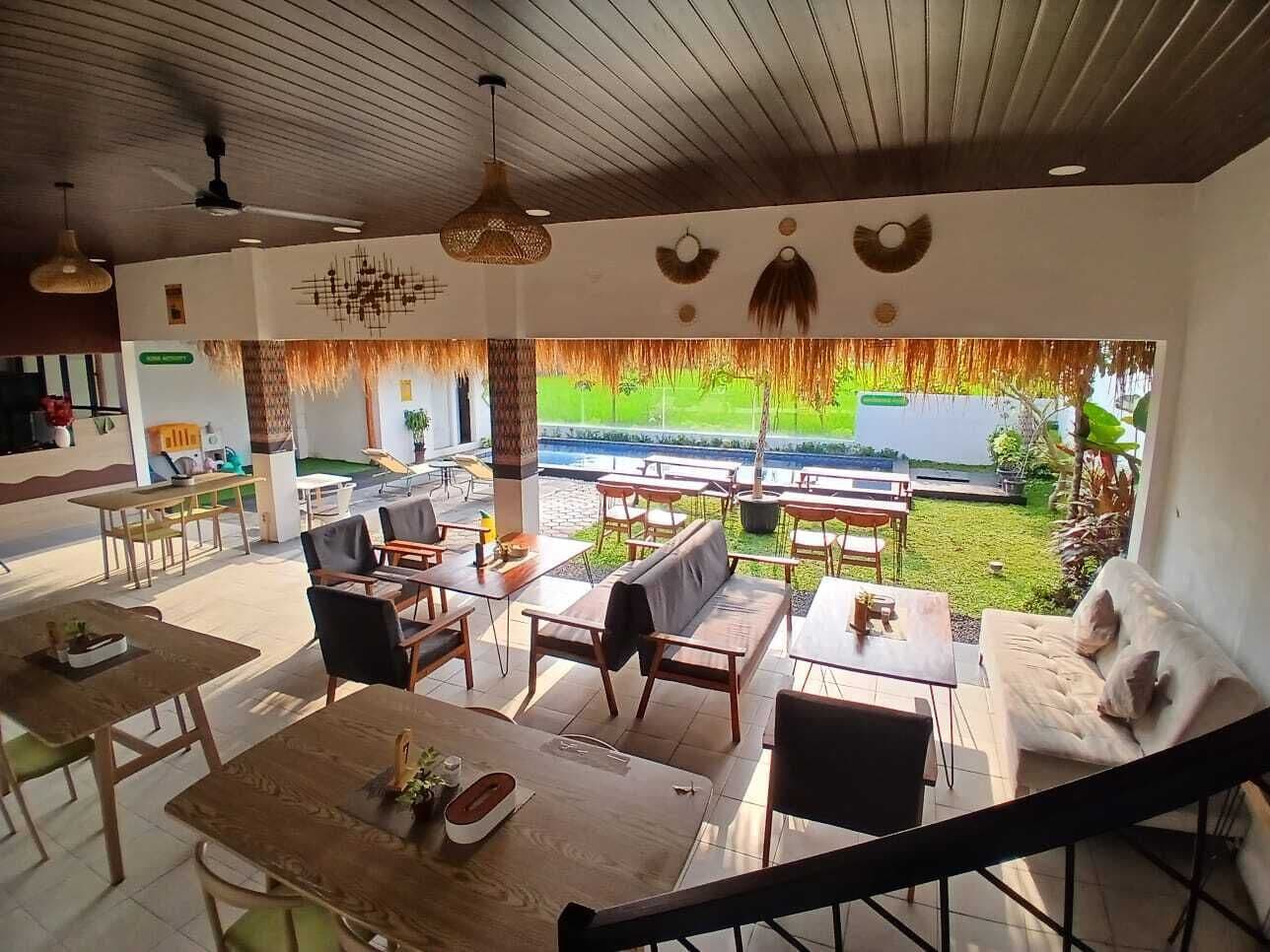 A spacious outdoor seating area with wooden tables and chairs, a sofa, and a grill.