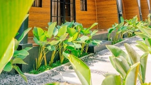 A modern building with a triangular roof design, large windows, and a garden area with tropical plants. - Dsvarga Glamping (Depok)