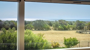 Vista desde una ventana que da a un paisaje costero con árboles y cielo despejado.