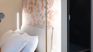 Un llit amb almoades blanques, un cortinat amb dibuixos florals i un mirall a la paret.