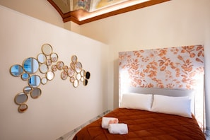A hotel room with a bed, a wall-mounted mirror arrangement, and a floral-patterned headboard.