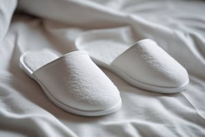 A pair of white slippers on a bed.