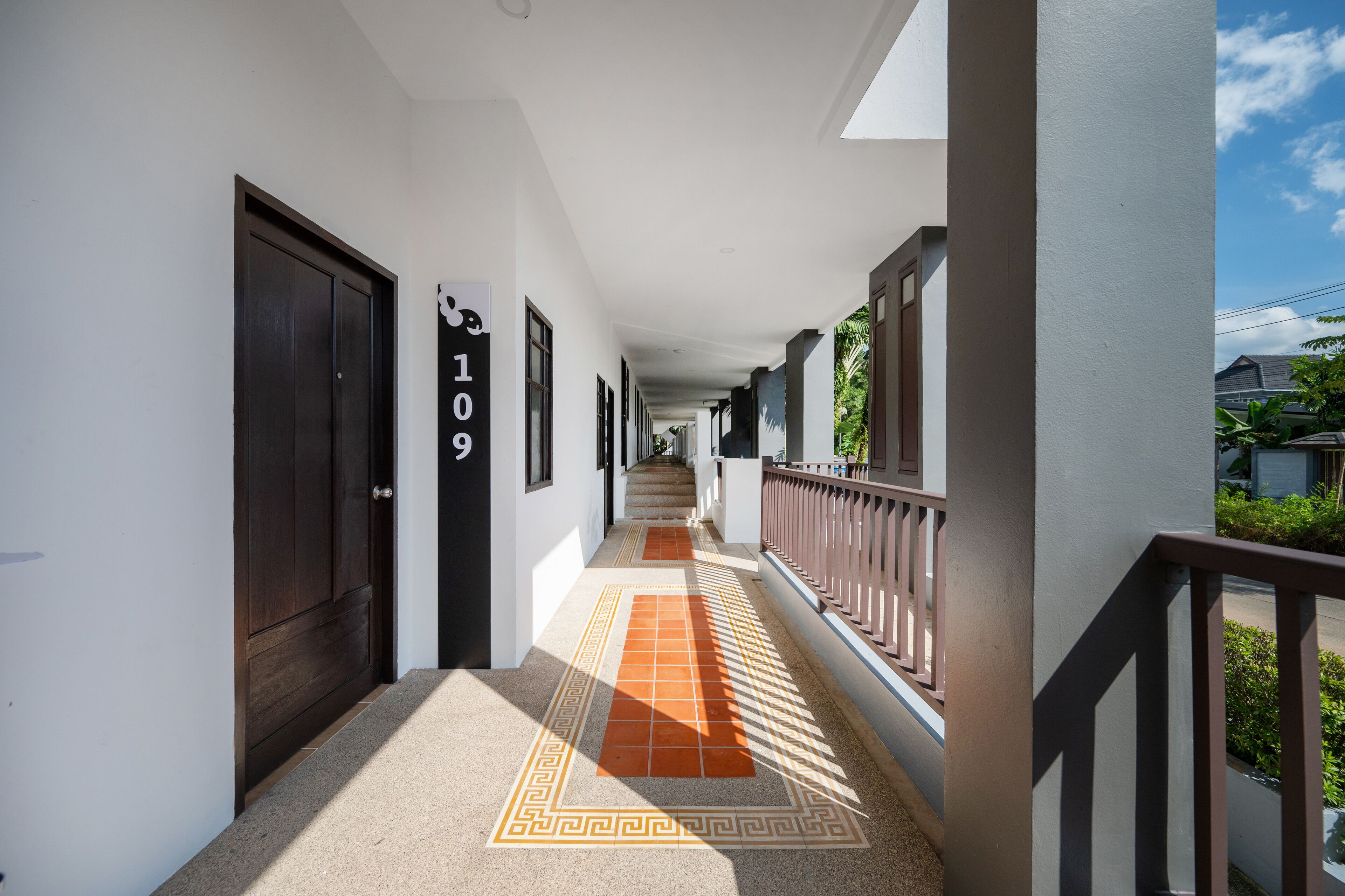 A corridor with a patterned floor, a balcony with a railing, and doors with numbers.