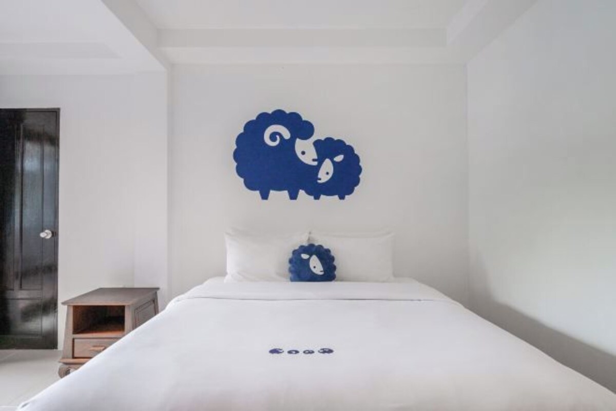 A bedroom with a bed, a nightstand, and a wall-mounted decorative sheep.