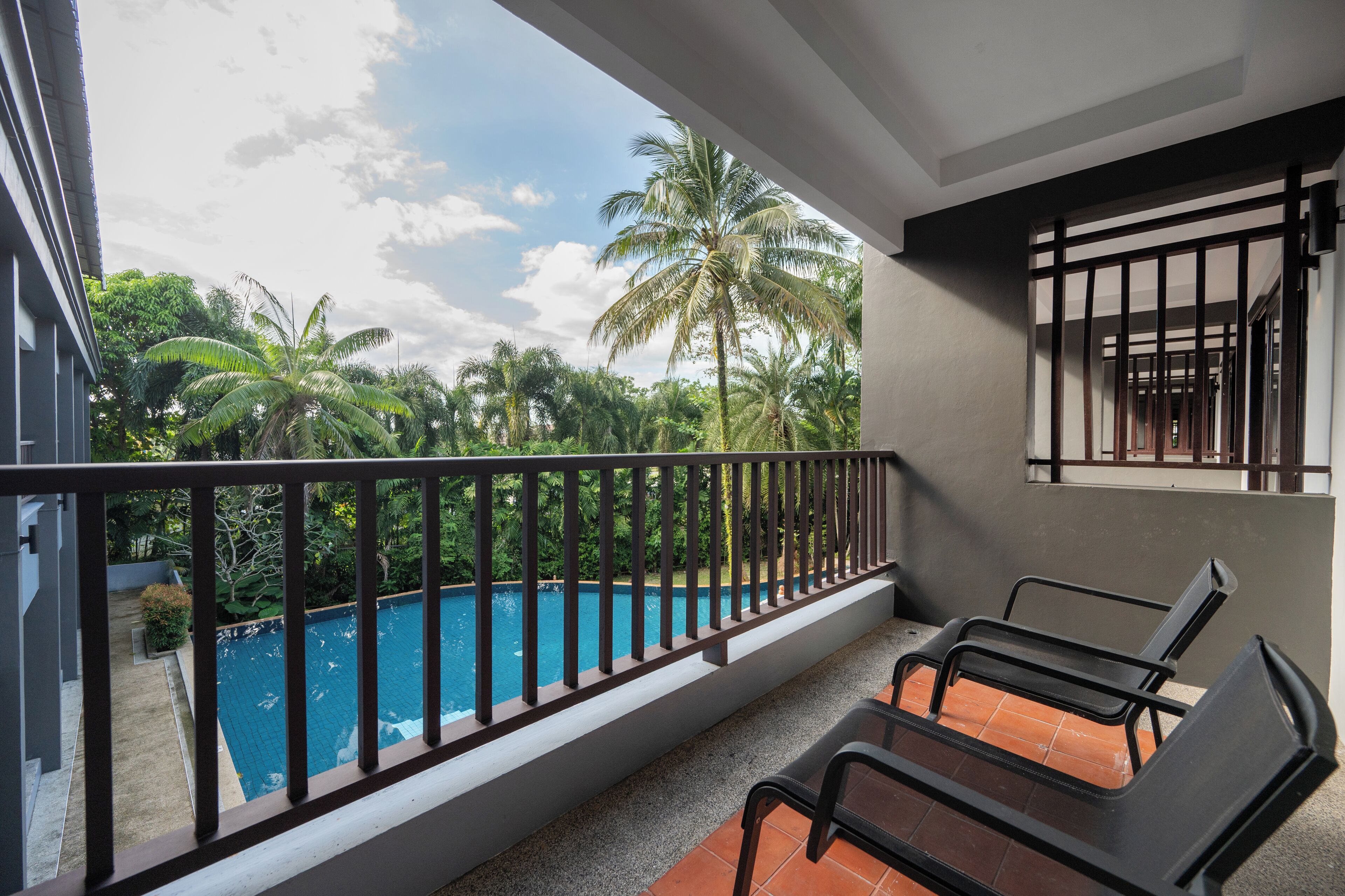 A balcony with a view of a swimming pool, surrounded by lush greenery and palm trees.