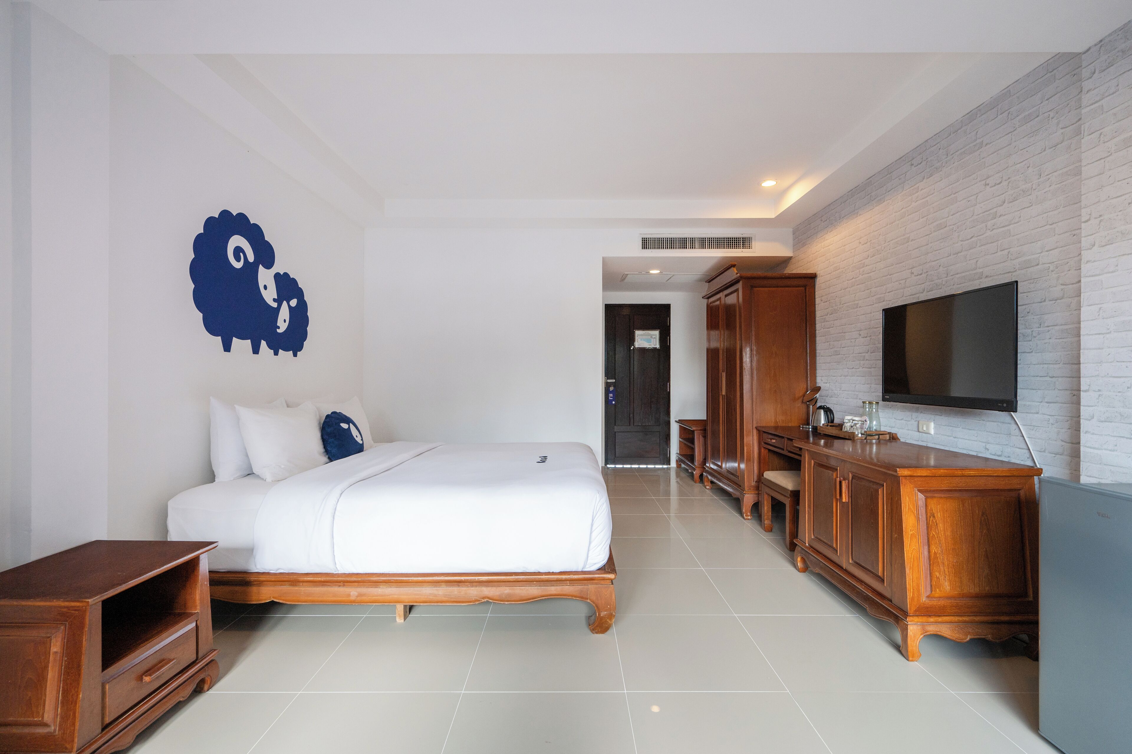 A modern hotel room with a bed, wooden furniture, a flat-screen TV, and a white brick wall.