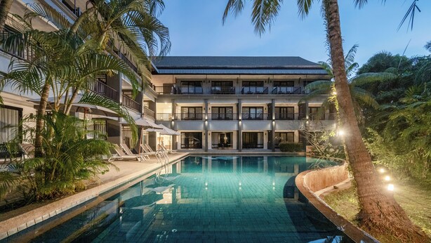 Ein Hotel mit Swimmingpool, Palmen und einem mehrstöckigen Gebäude mit Balkonen.