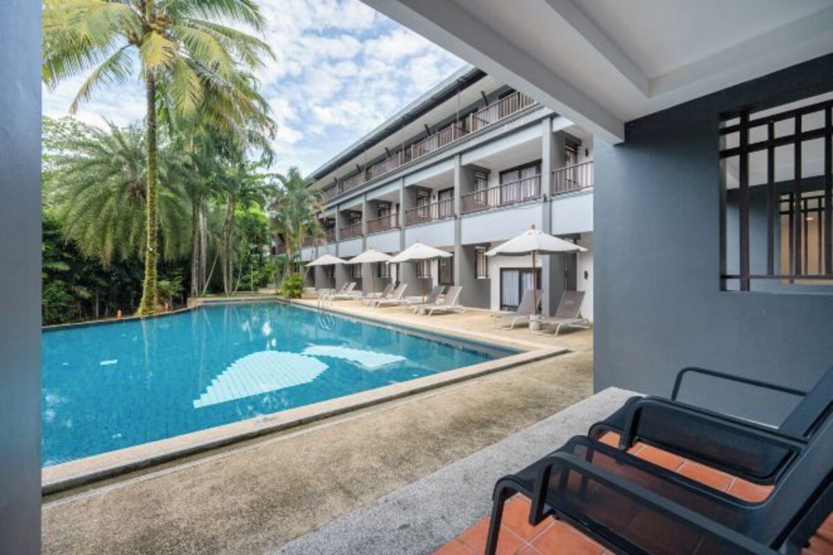 Un hôtel doté d’une piscine, de chaises longues et d’un bâtiment à deux étages avec des balcons.