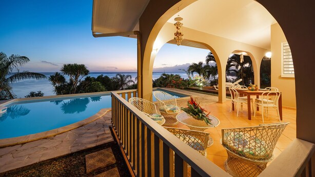 Un espace aménagé au bord de la piscine avec vue sur l’océan, une table à manger avec des chaises et un luminaire suspendu.
