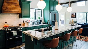 A kitchen with green cabinets, a large island with bar stools, a stove, and a refrigerator. - Duck Creek Luxury Cabin w/ Hot Tub | Las Hermanas (Kane County)