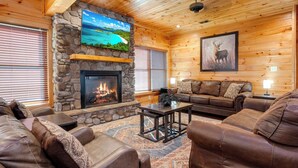 L’intérieur chaleureux d’un chalet en bois, avec une cheminée en pierre, des canapés en cuir et un grand tableau représentant un cerf.