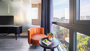 A modern hotel room with a large window, a black desk, an orange chair, and a small table with a book and flowers. - Greenview City Hotel (Xuan Huong - Da Lat)