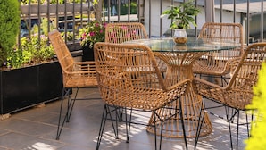 An outdoor patio with wicker chairs and a glass table, surrounded by potted plants and a metal fence. - Greenview City Hotel (Xuan Huong - Da Lat)