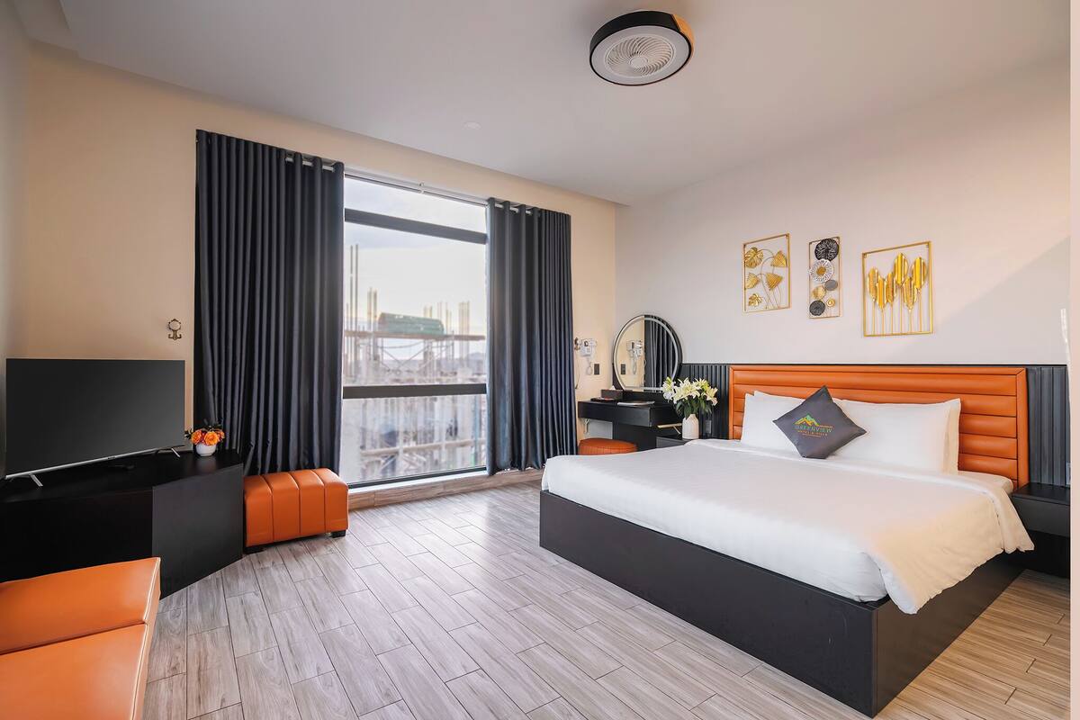 Habitación de hotel moderna con una cama grande, un televisor de pantalla plana, un escritorio y vistas a la ciudad a través de amplias ventanas.