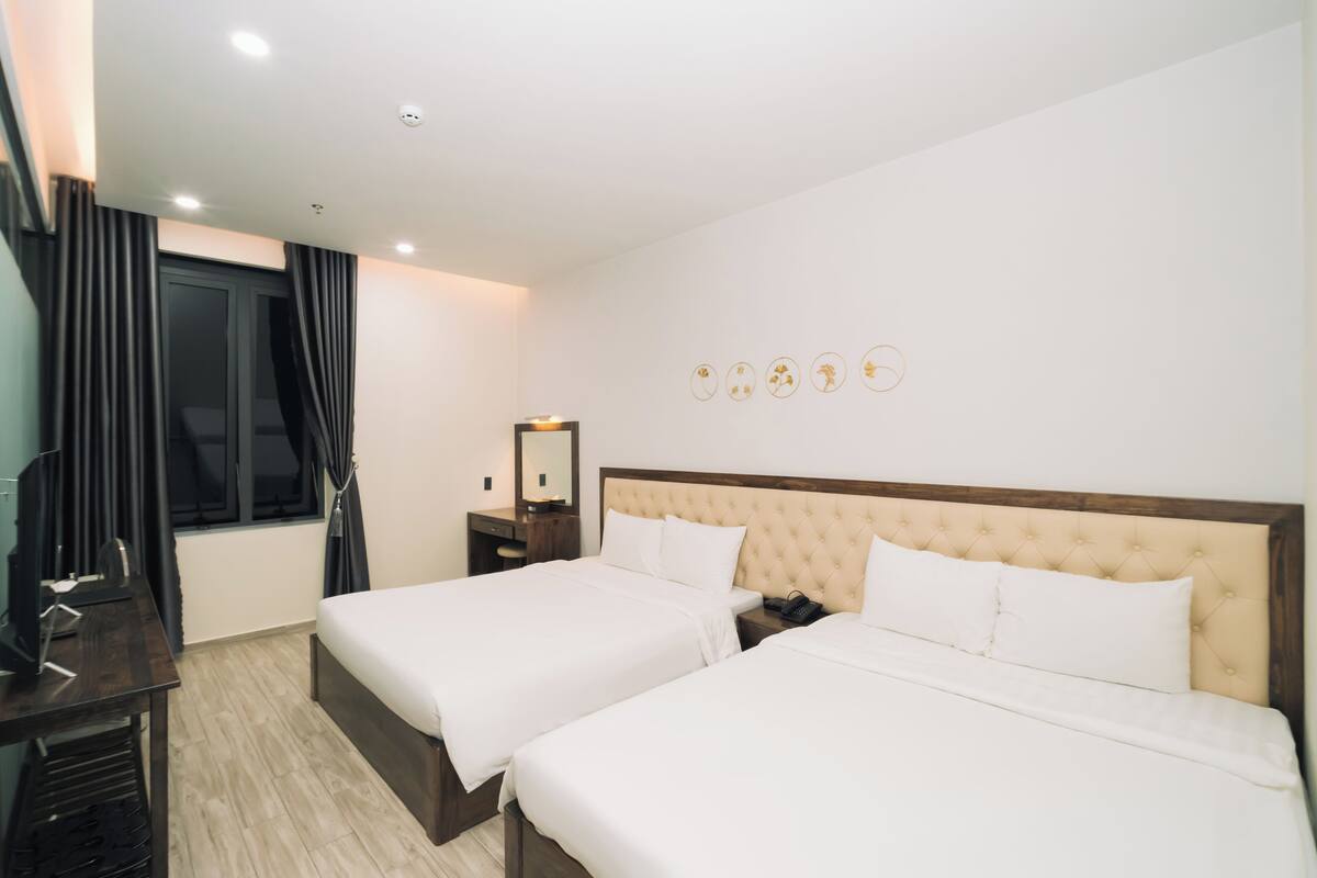 Una habitación de hotel con dos camas, un escritorio, un espejo y una ventana con cortinas.