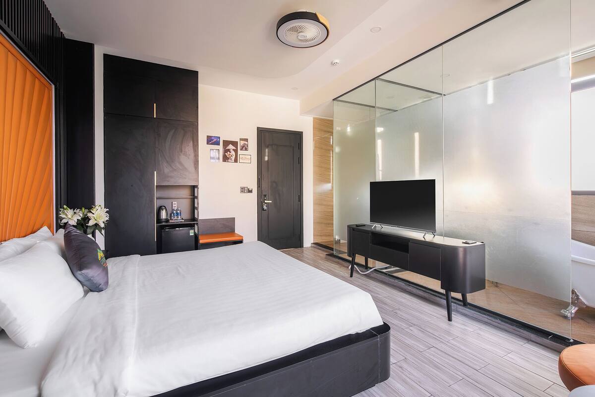 Una habitación de hotel moderna con una cama grande, un escritorio, un televisor de pantalla plana y un box de ducha de vidrio.