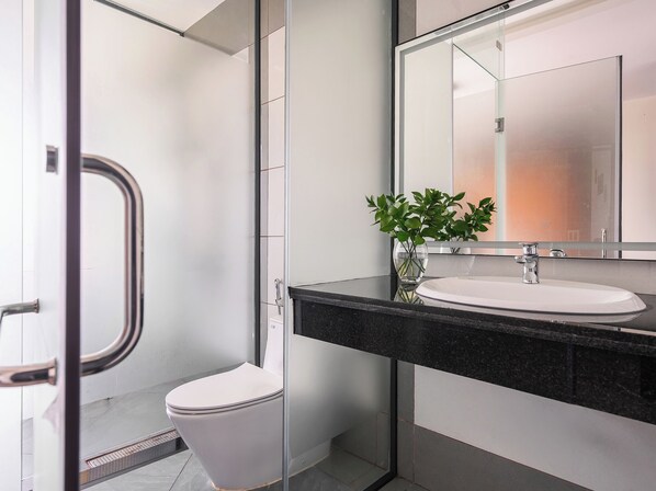 A modern bathroom with a glass shower enclosure, a white toilet, and a black countertop with a white sink and a mirror above it. - Greenview City Hotel (Xuan Huong - Da Lat)