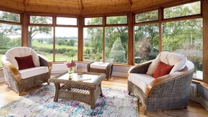 Een zonnehuis met rieten meubels, grote ramen en uitzicht op een groen landschap.