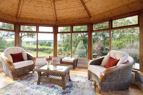 A sunroom with wicker furniture, large windows, and a view of a green landscape.