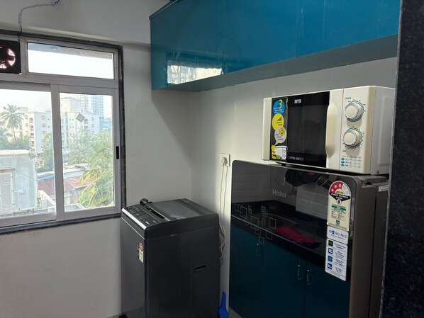 A compact kitchen with a toaster, a refrigerator, and a window with a view of buildings and trees.