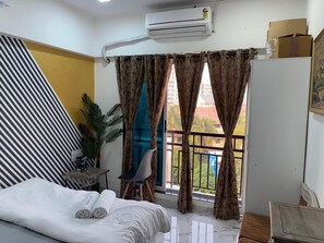 A hotel room with a bed, a chair, a small table, and a balcony with curtains.
