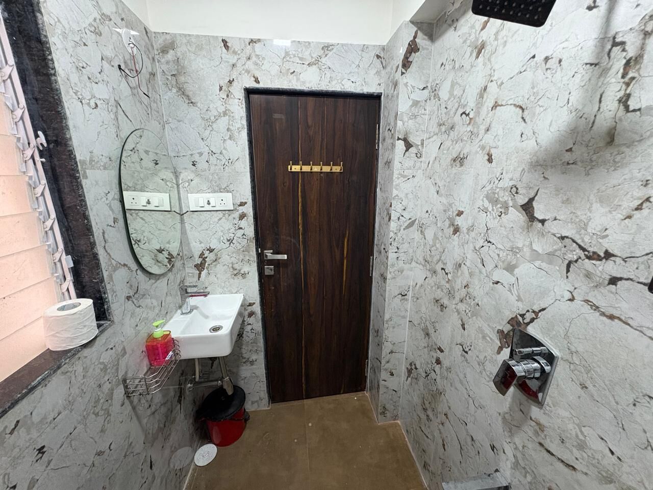 A bathroom with a marble wall, a wooden door, a white sink, and a mirror.