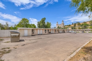A row of motel-style buildings with a large parking lot in front.