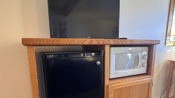 Een kleine keuken met een zwarte koelkast, een magnetron en een flatscreen televisie op een houten aanrecht.