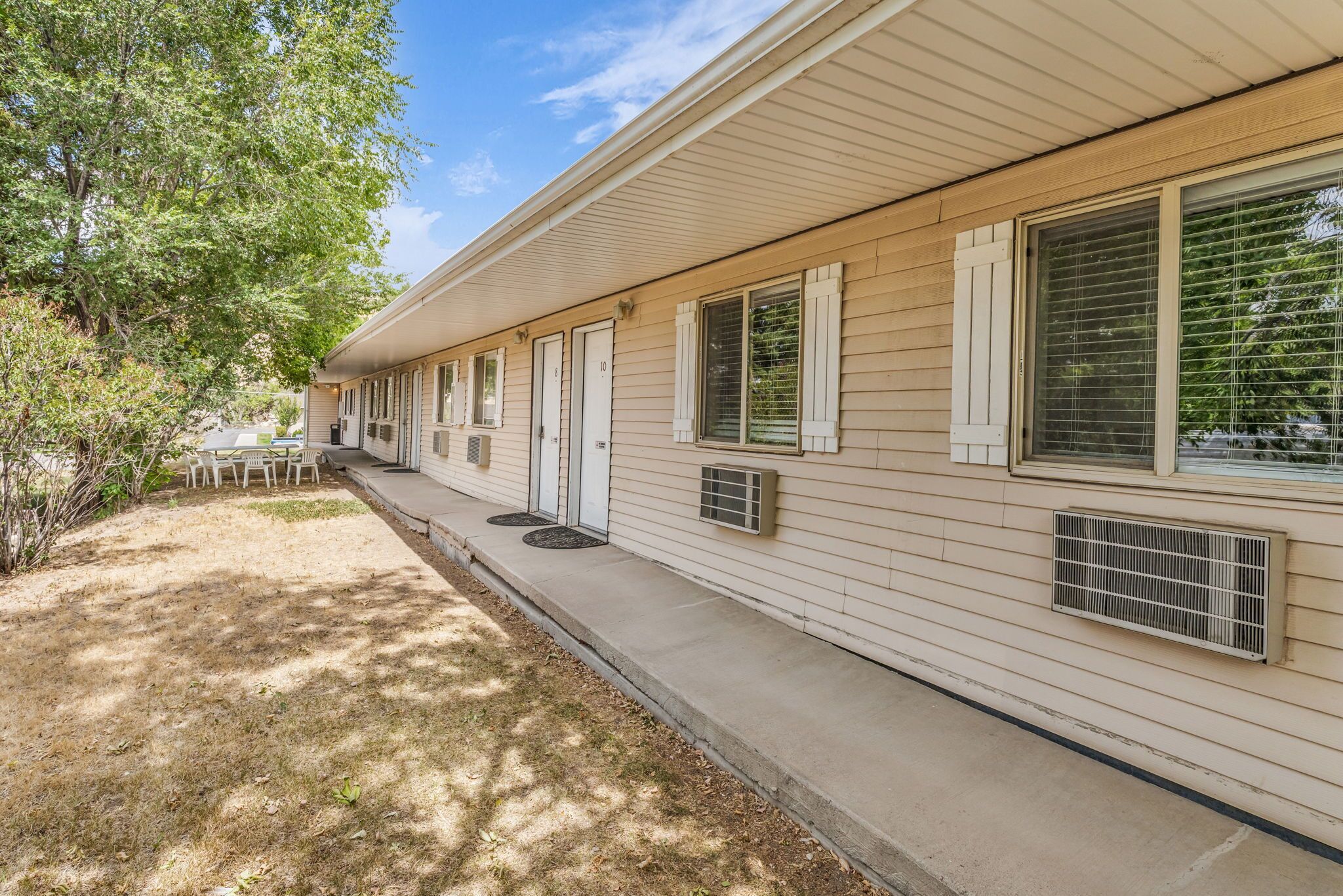 A row of single-story mobile homes with individual doors, each numbered, and a small patio area with outdoor furniture.