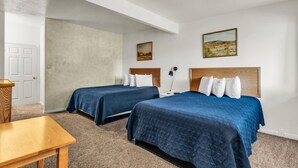 Hotellihuone, jossa on kaksi sänkyä, työpöytä ja ovi.