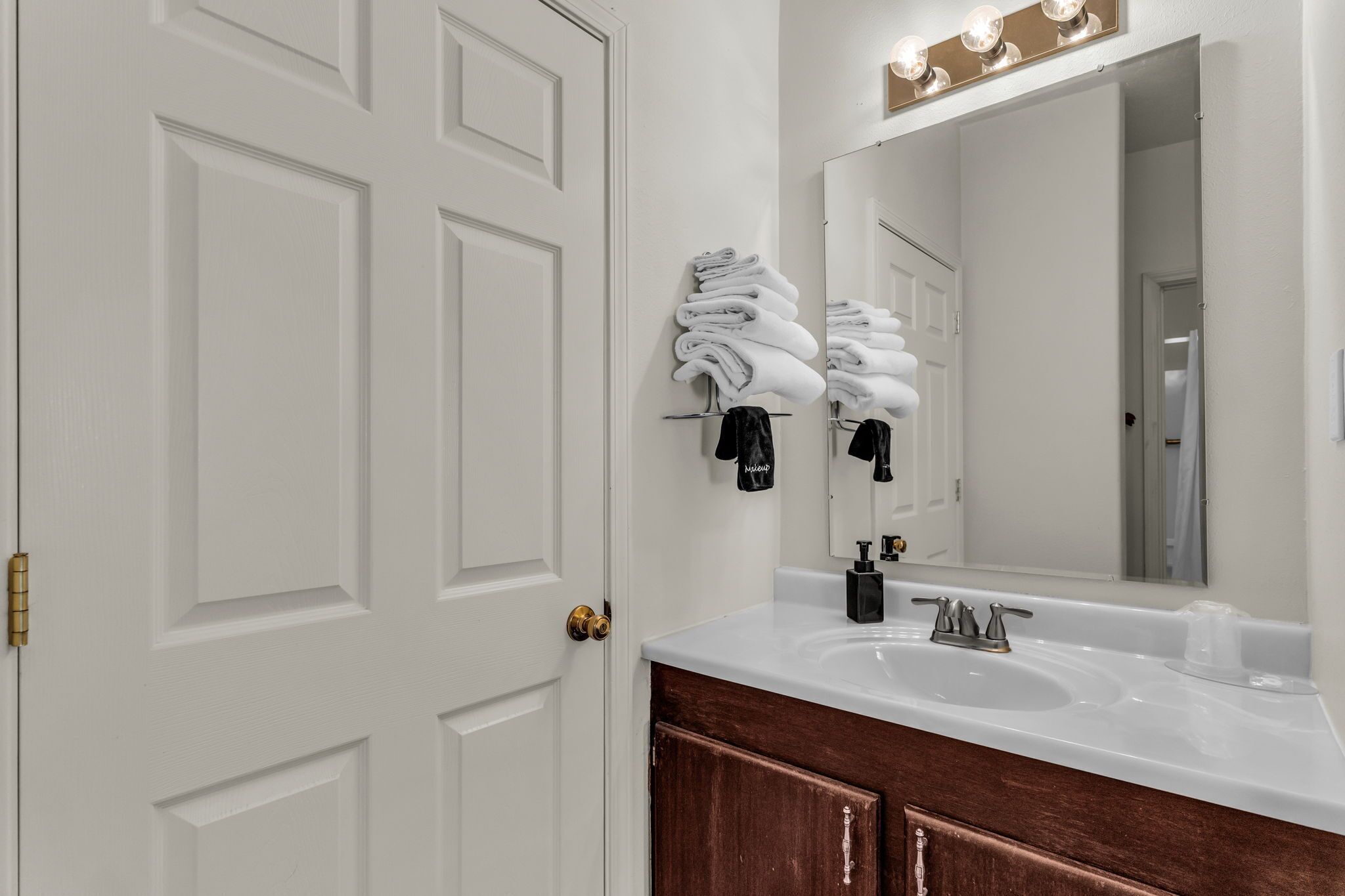 Une salle de bain avec une porte blanche, un lavabo surmonté d’un miroir et des serviettes suspendues à un porte-serviettes.