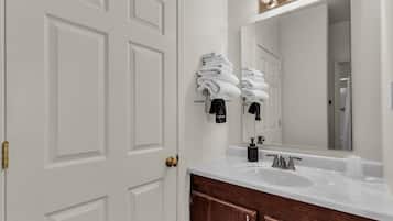 Un baño con una puerta blanca, un lavamanos con un espejo encima y toallas colgadas en un perchero.