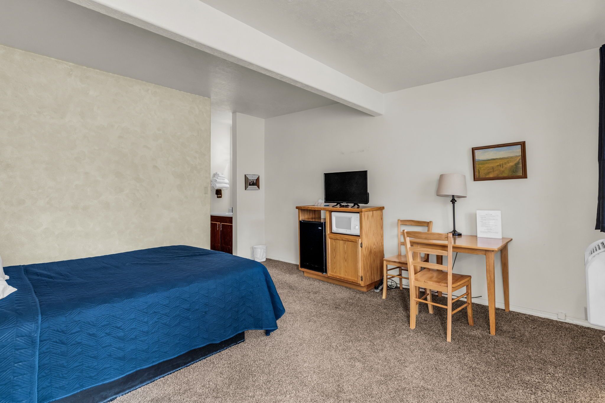 A hotel room with a bed, a desk with a computer, a television, and a painting on the wall.
