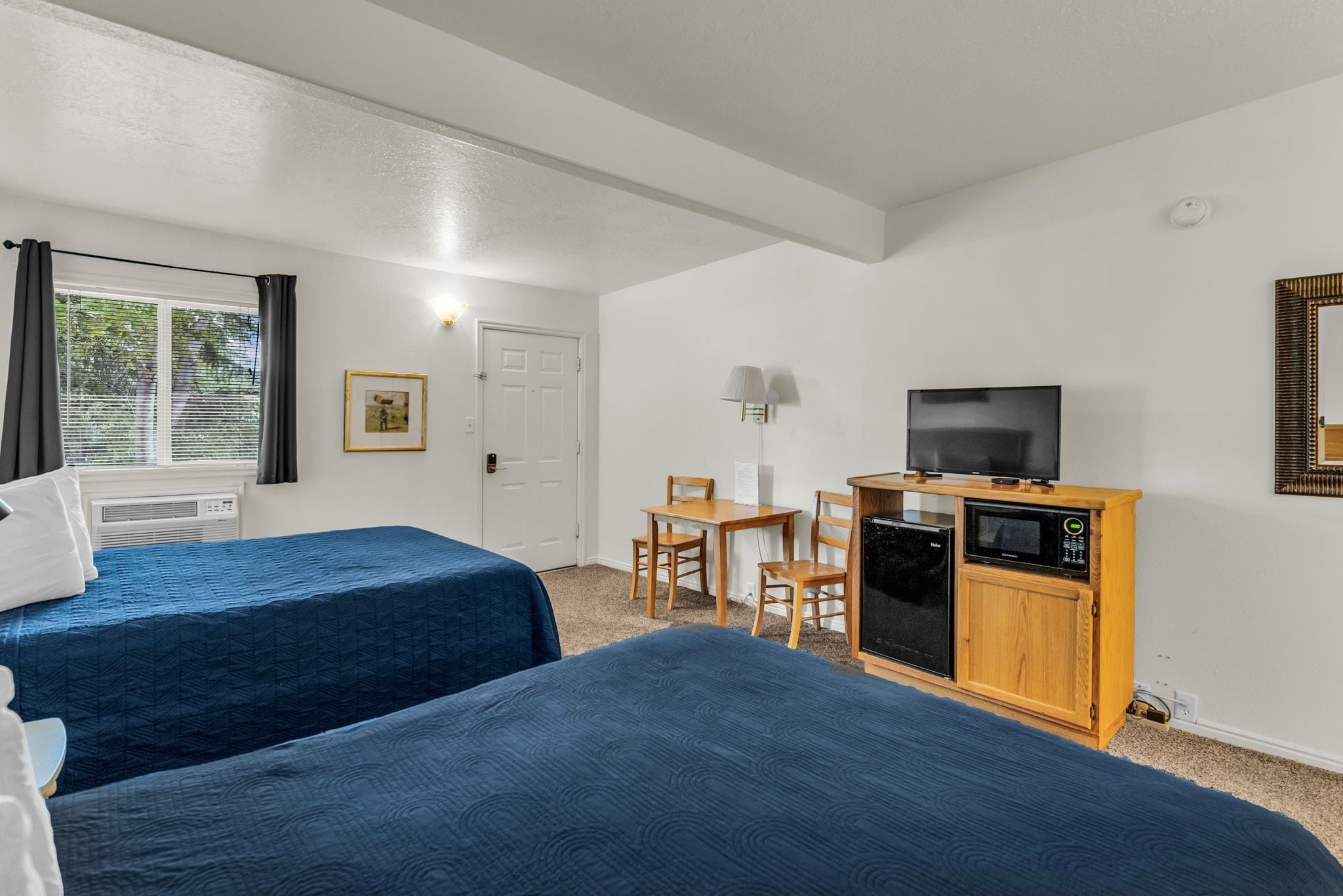 A hotel room with two beds, a desk with a chair, a television, and a microwave.