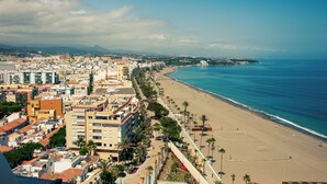Un paysage urbain côtier avec une vaste plage, des immeubles denses et une montagne à l’horizon.