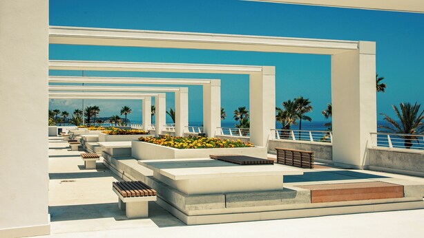 Un espace extérieur moderne, aménagé avec des structures et des bancs blancs, offrant une vue dégagée sur un ciel bleu azur et une perspective lointaine sur la mer.