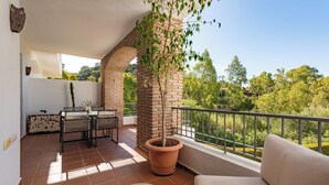 Ein Balkon mit einer Ziegelstütze, einem Blumentopf, einer Couch und einem Essbereich mit Stühlen und einem Tisch.
