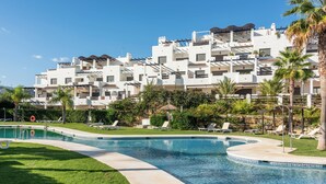 Una piscina con sillas de descanso y un edificio blanco con balcones al fondo.