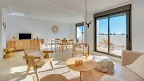 Una sala de estar moderna con un ventanal grande, un comedor y un televisor sobre un mueble de madera.