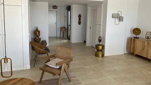 Un amplio espacio de sala con sofá, sillas y una mesa de centro. Hay una lámpara decorativa y una consola con un florero.