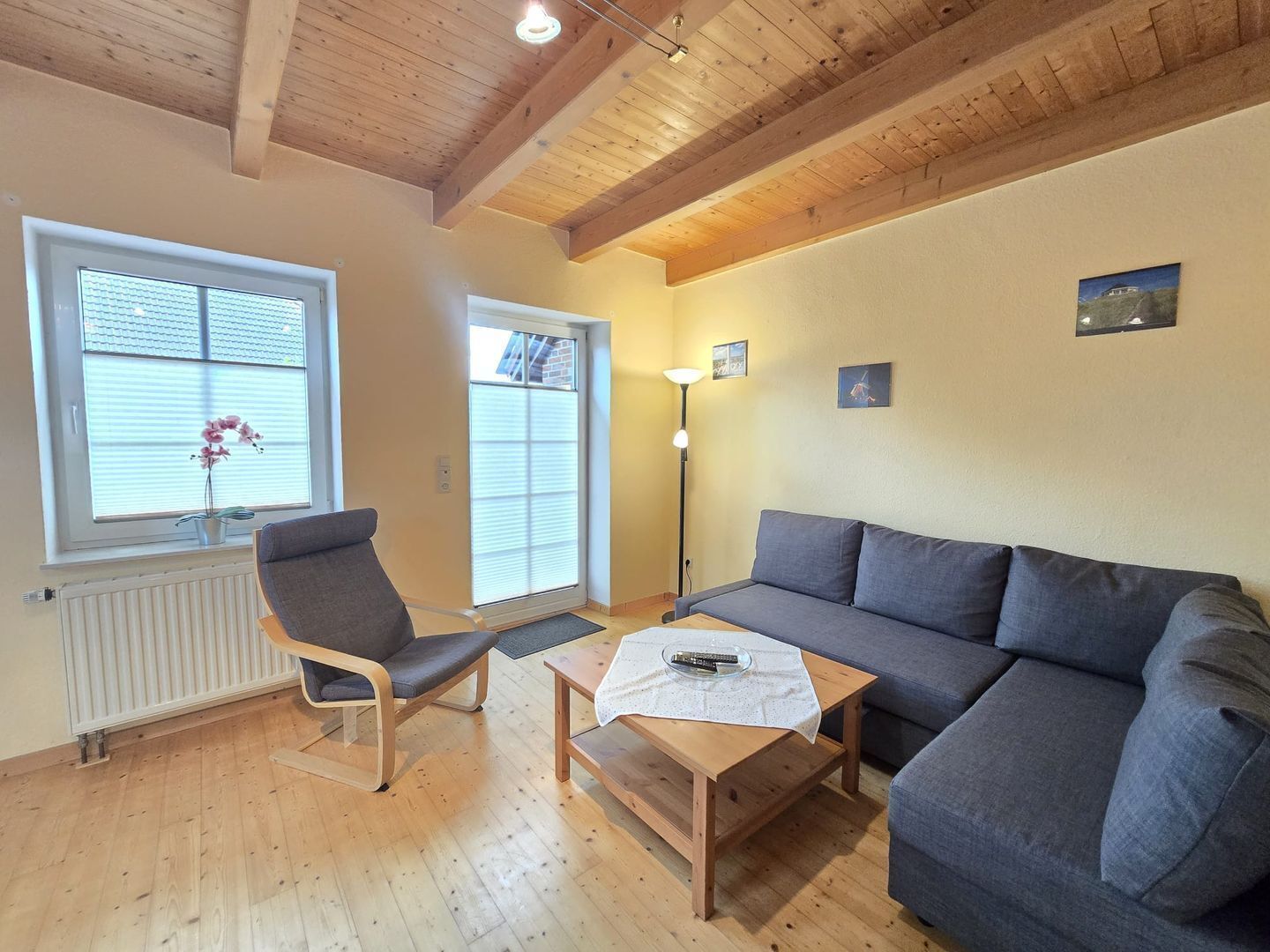 Ein gemütliches Wohnzimmer mit Holzboden, einem grauen Sofa, einem Holzstuhl, einem kleinen Tisch und einer Heizung.