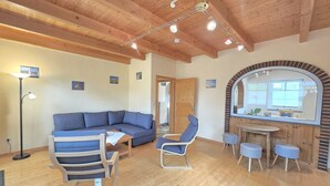 A cozy living room with a blue sofa, a striped chair, a small table, and a wooden ceiling. - Apartment Nordseeperle - Comfortable apartment Nordseeperle with garden, (Dornum)
