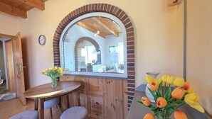 A wooden dining area with a round table, two stools, and a mirror with an arched brick frame. - Apartment Nordseeperle - Comfortable apartment Nordseeperle with garden, (Dornum)