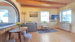 A cozy living room with a wooden ceiling, a large mirror, a dining area with a table and chairs, a TV, and a window with a view of the outside. - Apartment Nordseeperle - Comfortable apartment Nordseeperle with garden, (Dornum)