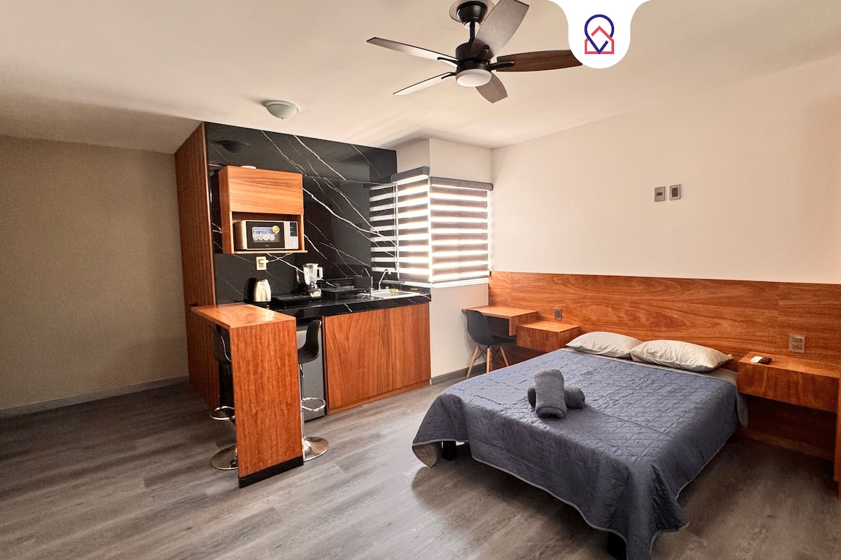 Une chambre compacte comprenant un lit, des tables de chevet, un bureau et un coin cuisine.