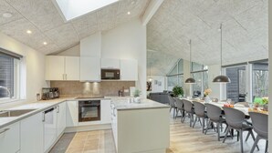 A modern kitchen with white cabinetry, a central island, and a dining area with grey chairs and a long table. - Stunning home in Jesendorf with sauna (Jesendorf)