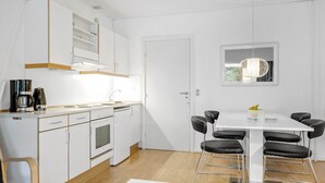 Una cuina moderna amb armaris blancs, una cafetera i una zona de menjador amb taula blanca i cadires negres.