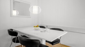 Zona menjador moderna amb taula blanca, cadires negres, un bol de fruita i una làmpada penjant.
