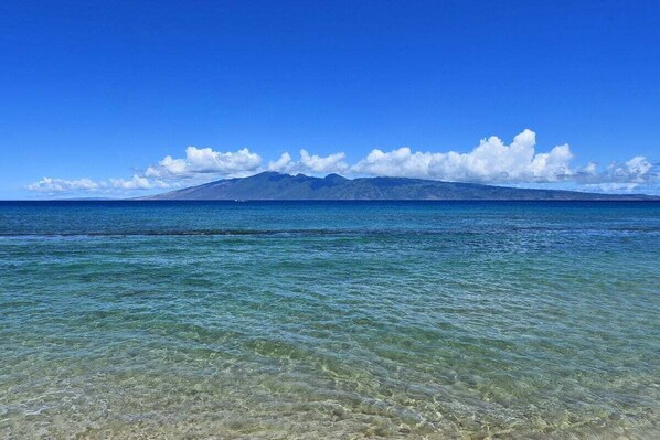 Una vista despejada de una playa con aguas tranquilas y una montaña a lo lejos.