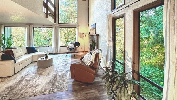 A spacious living room with a large window, a fireplace, and a cozy seating area. - Perch - Lake Forest Park Retreat (Kenmore)